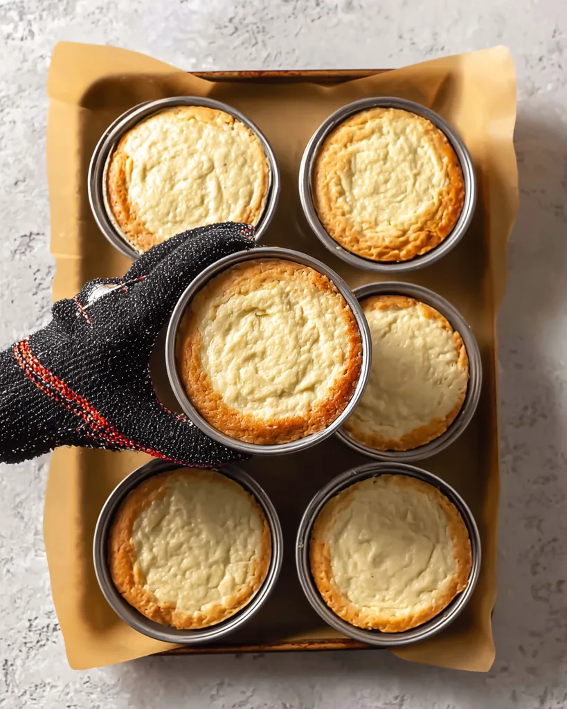 Thick almond flour batter scooped into six greased muffin rings on a baking sheet