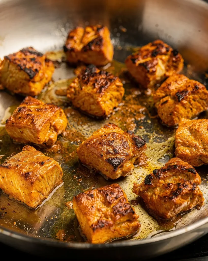 Bite-size marinated chicken pieces searing with charred edges in a stainless steel skillet