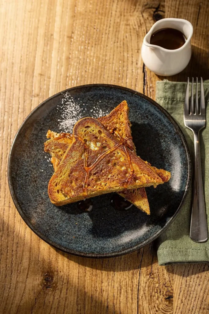 Plate of golden low-carb french toast triangles drizzled with syrup, with a pitcher of syrup and a fork