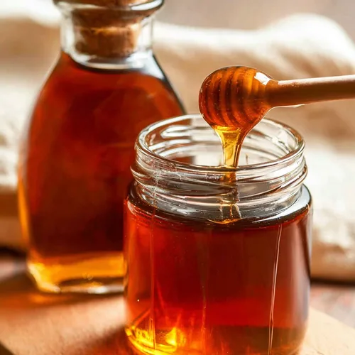 Keto maple syrup dripping from a wooden dipper into a jar, with a glass bottle behind