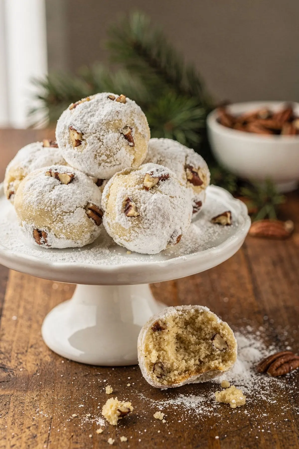 Keto snowball cookies on a white cake stand with one broken open to show the pecan crumb
