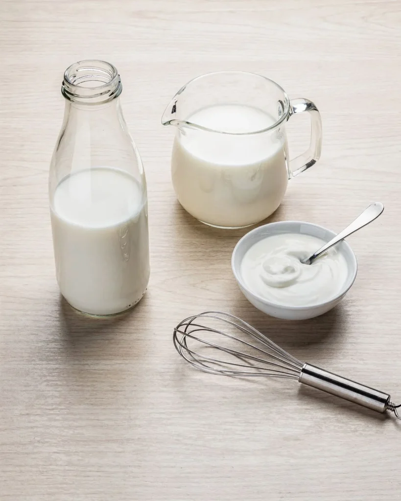 Milk, heavy cream and a small bowl of plain yogurt starter with a whisk